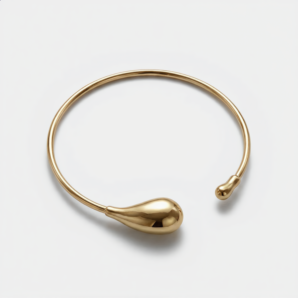 Gold bangle with teardrop design on a light gray background