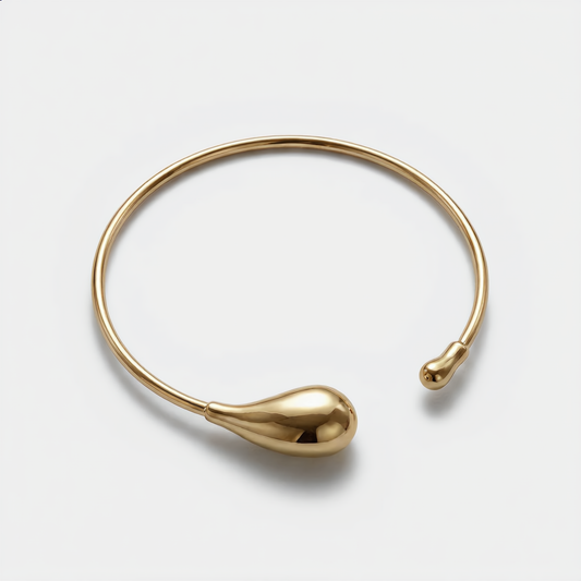 Gold bangle with teardrop design on a light gray background