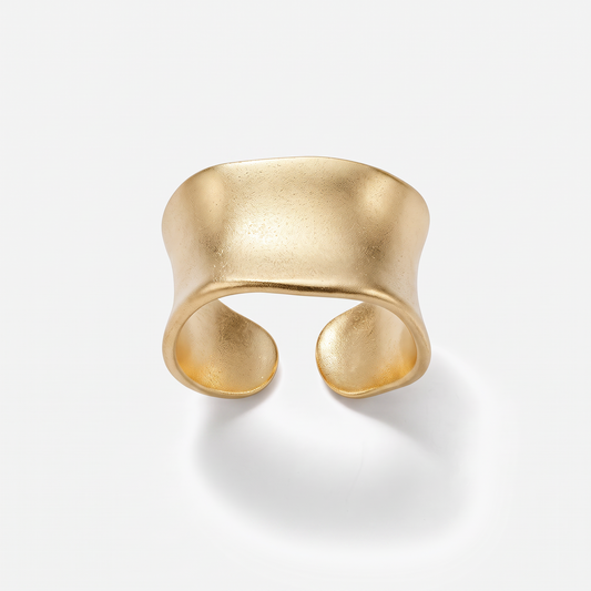 A wide, open cuff ring in matte yellow gold with a textured, organic wavy shape, photographed on a clean white background with a soft shadow.